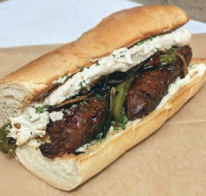 Homemade seitan sausage with sauteed peppers and onions and sunflower cheese and remoulade, Cauldron Collective